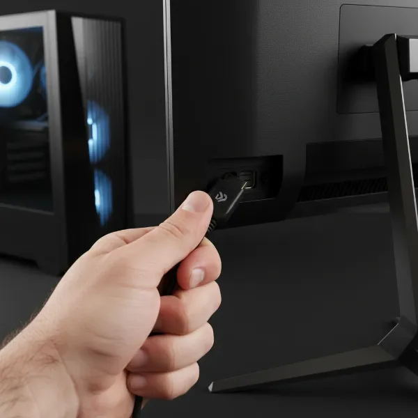 Hand securing loose HDMI or DisplayPort cables connecting a gaming monitor to a PC.